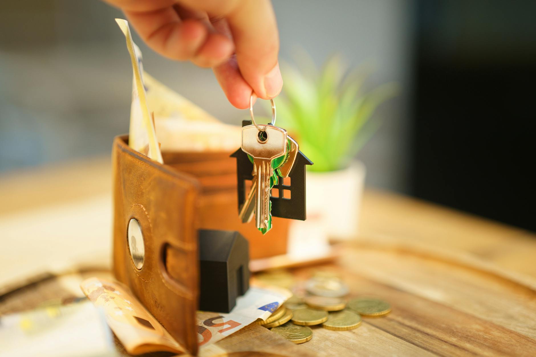 hand holding house key above wallet with coins