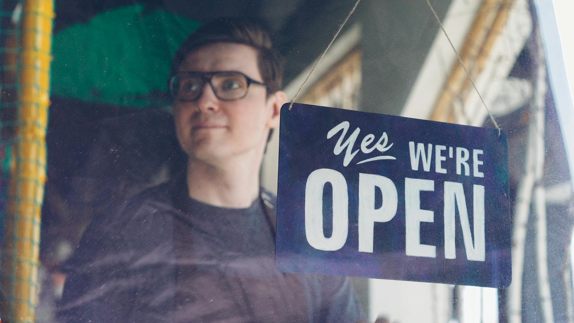 shop owner smiling behind open sign in window