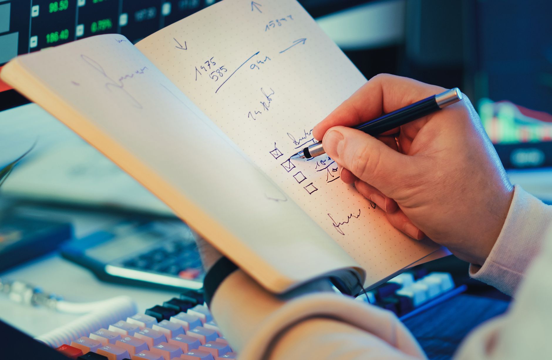 person writing in notebook for stock market planning
